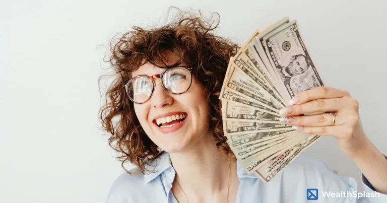 Smiling woman with curly hair and glasses holding dollar bills in front of a white background: how to make money fast as a woman