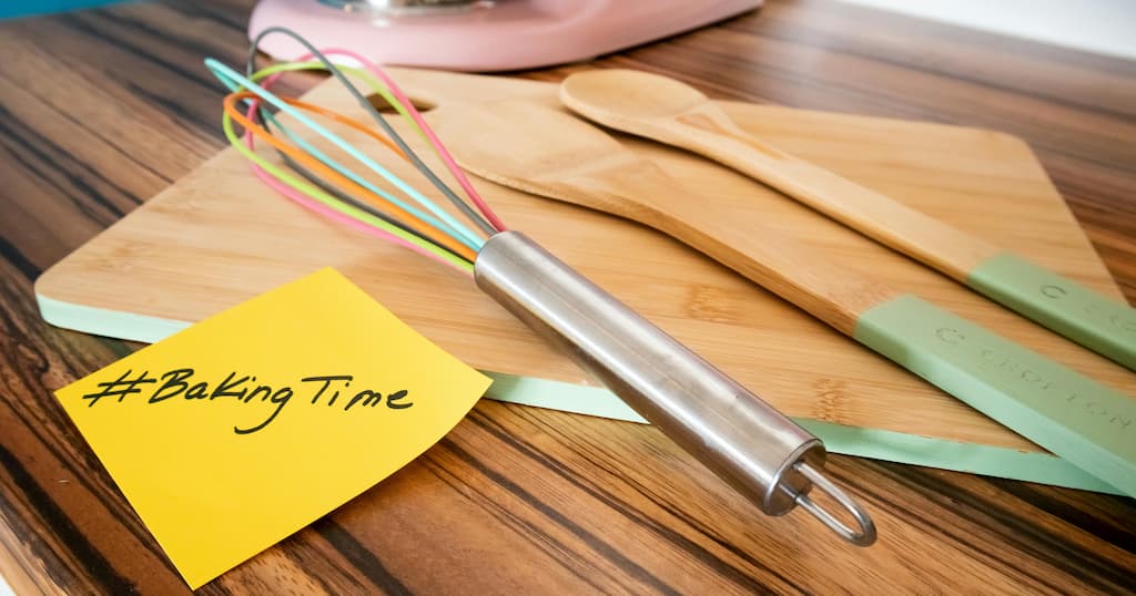 Colorful metal whisk and kitchen tools on a wooden board with a note reading #BakingTime