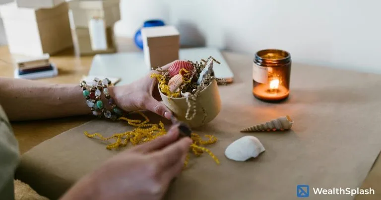 Hand placing seashells on craft paper beside a lit candle in a peaceful, creative workspace: things to make and sell